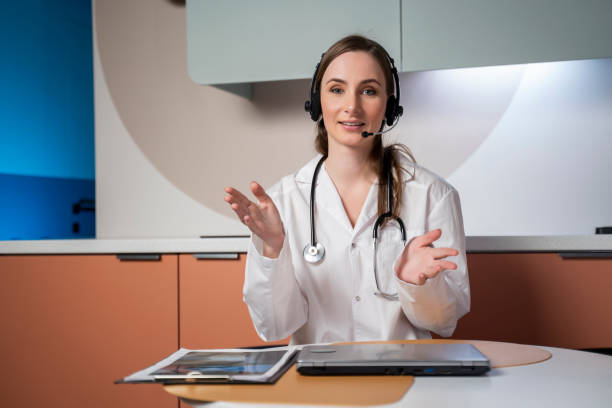 istock Young female doctor in a white medical uniform with a stethoscope, using a computer laptop, talks via videoconference with a patient, looking into the camera at a healthcare hospital 1480842182