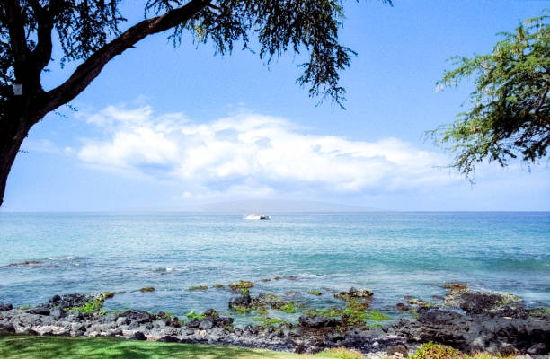 A scenic view of the ocean with a sailboat in the distance, set against a backdrop of a mountainous island and a partly cloudy sky.
