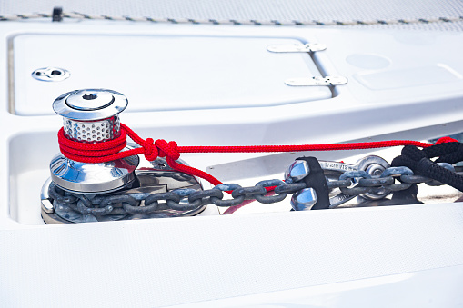 Winch on a yacht with an anchor chain and tied red rope.