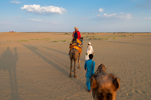 Thar desert, Rajasthan, India- 15.10.2019 : Female tourist riding camel, Camelus dromedarius, at sand dunes of Thar desert, Rajasthan, India. Camel riding is a favourite activity amongst all tourists.