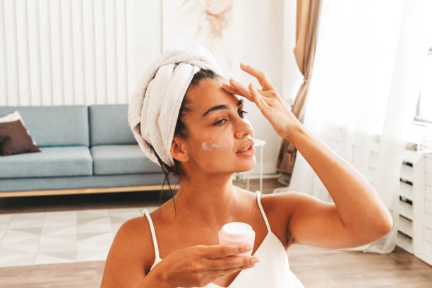 istock Charming brunette woman with towel wrapped on her head applying moisturizing face cream 1480851568