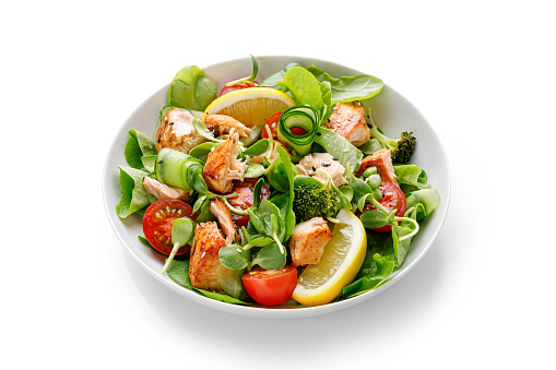 Healthy salad with pieces of baked salmon and green lettuce and tomatoes isolated on white background with clipping path. Fresh diet dinner meal. Fish summer salad. Vitamin food concept.