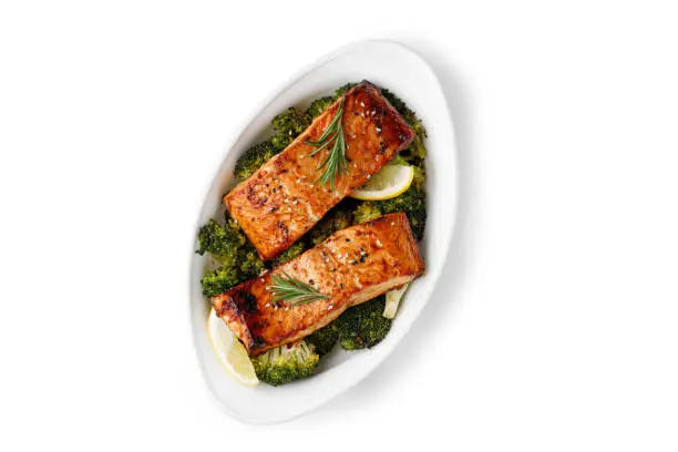 Photo of Salmon. Baked, roasted fish steaks, slices. Grilled salmon, trout fillet fish in marinade with broccoli in baking dish isolated on white background. Diet, meal, dinner.