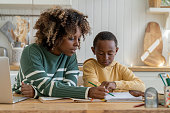 Homeschooling biracial pupil boy with help of personal tutor woman. Pensive son do homework with mom