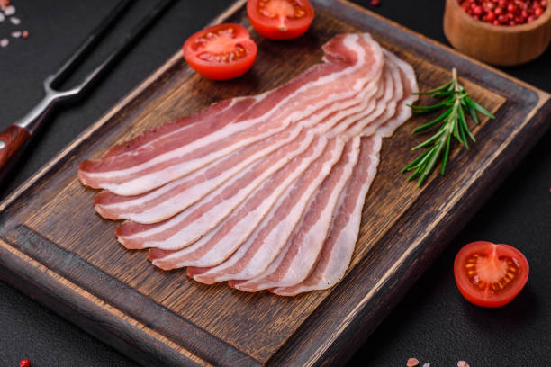 Delicious fresh pancetta with salt and spices cut into thin slices Delicious fresh pancetta with salt and spices cut into thin slices on a dark concrete background uncooked bacon stock pictures, royalty-free photos & images