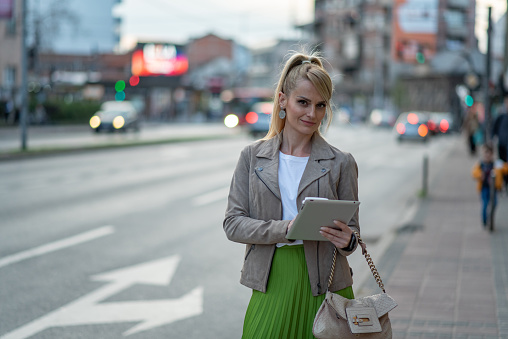 Business woman on a coffee break walking down the street. She is holding tablet and a cup of coffee.
