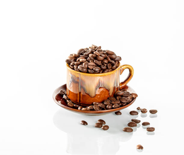 istock Coffee theme. A ceramic cup filled to the brim with coffee beans stands on a white mirror background 1480857493