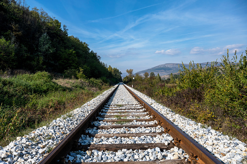 Infrastructure development project with laying of railway tracks equipped with overhead electric poles in parallel to high powered supply lines in dry terrain during summertime