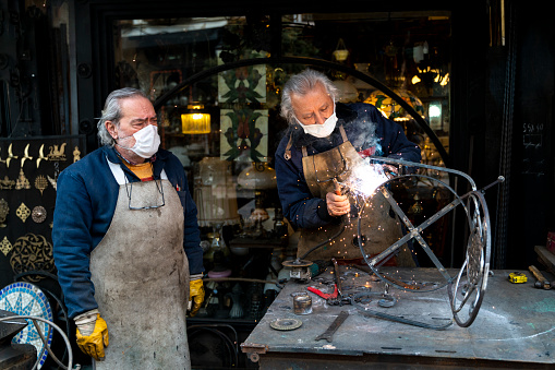 old blacksmiths photographed working. they have a protective mask in their mouth. master carefully welds. Shot in natural light with a full-frame camera.