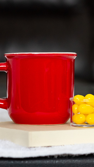 Yellow mug turned sideways on wooden coaster with small container of yellow jelly beans, black background