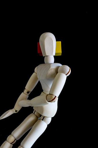 Wooden figure laying on black background, with red and yellow blocks as a pillow