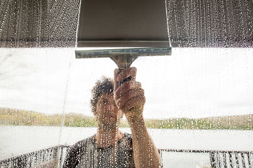 Looking through a soap covered window at a man using a squeegee to clean the exterior windows of a house.