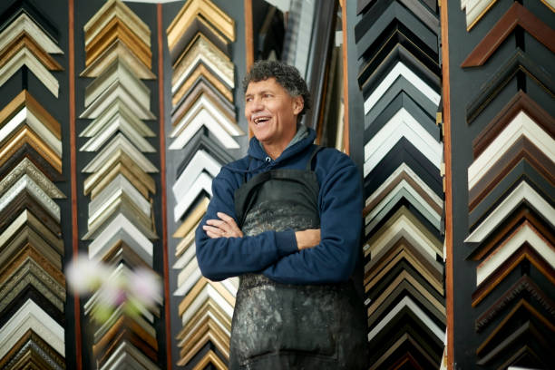 Painting, frame and art with a man designer laughing in his workshop for creative or modern decor. Selection, design and retail with a male artist at work as a painter alone in his artistic studio