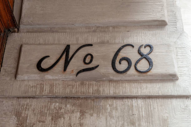 68 numerals in steel painted black fixed against a cream brick wall.