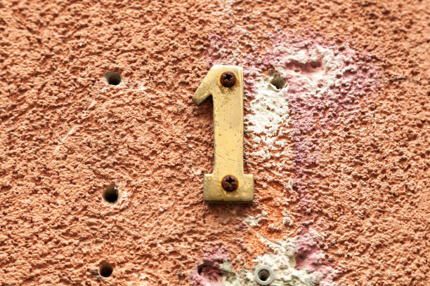 istock 1 numerals in bronze fixed against a orange painted rendered brick wall with evidence of house numbering repairs. 1480895612