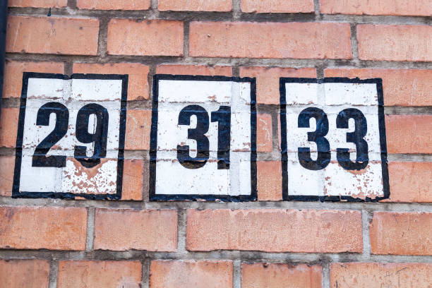 istock 29 31 33 number decorative font in black paint against white painted shield handpainted on house wall of red tones brick. 1480895649