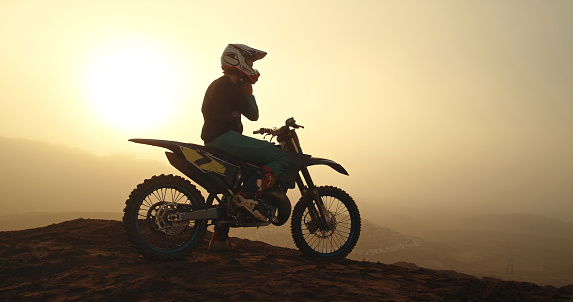 Bike, sports and motocross with a man rider enjoying rally, motogp or xcross outdoor in nature at sunset. Motorbike, ride and adrenaline with a male biker on a hill or mountain for sport recreation