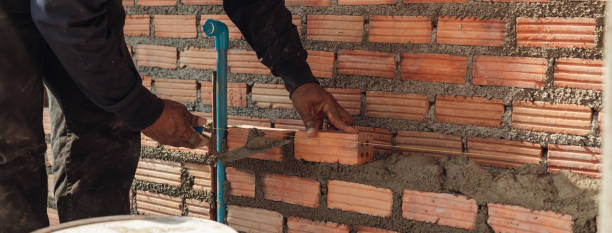 istock Bricklayer with trowel to installing red bricks masonry and  PVC pipe in a new wall. 1480897412