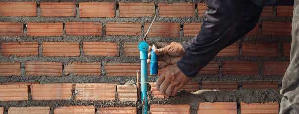 istock Bricklayer with trowel to installing red bricks masonry and  PVC pipe in a new wall. 1480897438