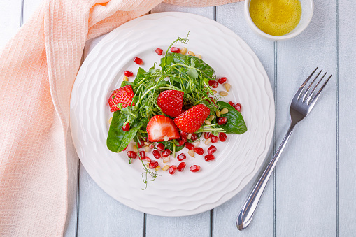 Salad with microgreens, strawberries, pine nuts and pomegranate seeds. On a white wooden background