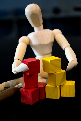 Wooden figure playing with red and yellow blocks with black background