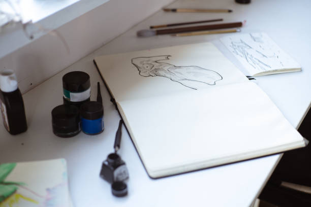 スケッチブック、ペン、黒インクを持つアーティストの創造的な職場。 女性アーティストスタジオ