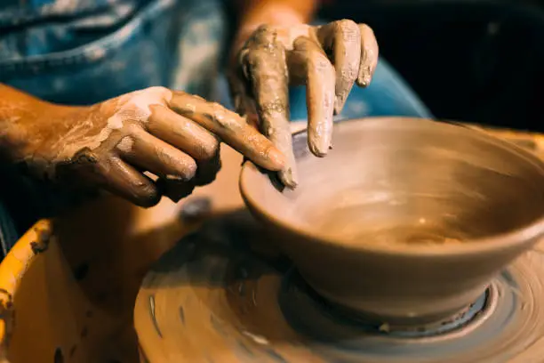 Professional craftsman potter making jug of clay on potter wheel circle in workshop, Traditional handicraft working, Creativity and art of pottery, Artisan working with wet clay decorating and shaping jug before baking in pottery studio