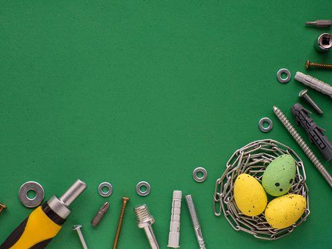 Easter eggs on green background with hand tools, fasteners and fittings. Easter card design with copy space. A nest for an egg made from metal chain. Easter tools, worker concept.