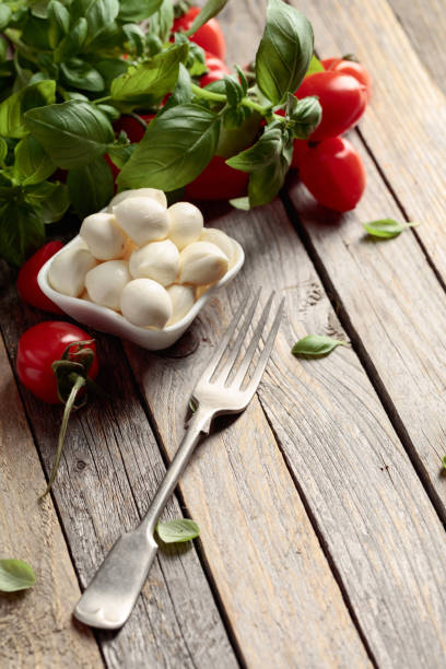 Mozzarella cheese with basil and tomatoes on an old wooden table. Traditional Italian snack.