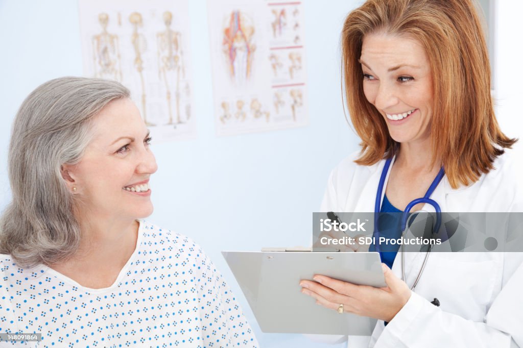 Счастливый доктор писать с ее пожилой возраст пациента - Стоковые фото Больничная рубашка роялти-фри