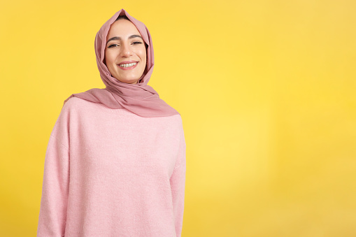Happy muslim woman smiling at the camera in studio with yellow background