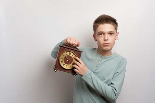 A boy holding original wooden retro clock with roman numbers and arrows showing the time