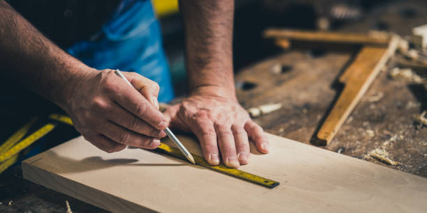 Carpenter measuring wood with meter instrument Male carpenter measuring wooden plank using meter instrument and pencil in woodshop carpenter stock pictures, royalty-free photos & images