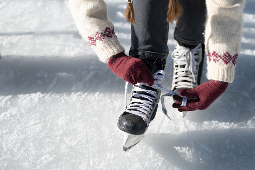 Woman tying ice skate shoelaces on frozen lake in natural parkland in winter close up top view