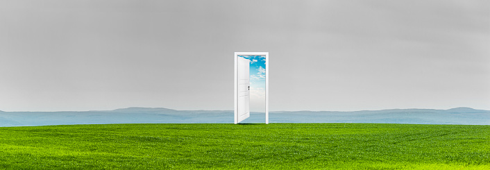 Open door in a green meadow in front of a hilly mountain panorama
