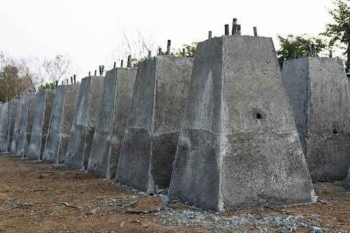 Numerous concrete pillar bases, which were built by cement casting in a steel box and lined up in rows, are left to dry on the ground in rural Thailand, waiting to be buried and assembled into street lampposts.