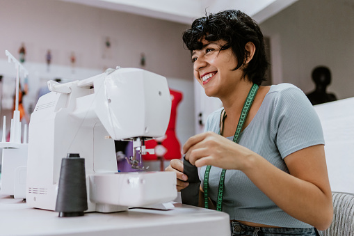 Joven diseñadora de moda latina trabajando con una máquina de coser en su taller en México América Latina photo