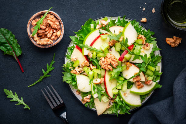 istock Waldorf salad with red and green apple, celery, lettuce, arugula and walnuts on plate, black table background, top view 1480943921