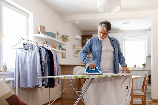 Housework and Household Concept - Man Ironing Shirt on Iron Board at Home