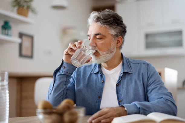 hombre bebiendo agua en casa - sediento fotografías e imágenes de stock
