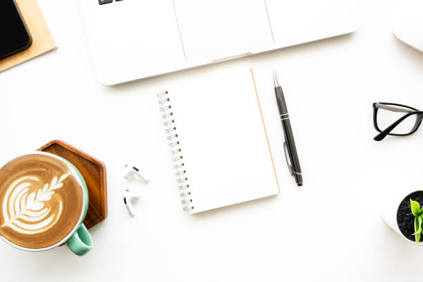 istock Blank notebook is on top of white office desk table with laptop computer and office supplies. Top view with copy space, flat lay. 1480946975