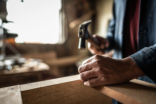 Close-up of man hammering a nail on piece of wood