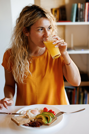 Relaxed young woman drinking juice while having breakfast at home