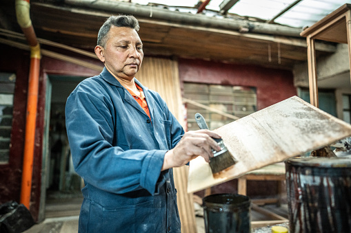 Mature man painting piece of wood at carpentry workshop