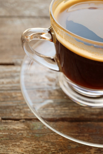 Hot black coffee in a transparent cup isolated on wooden table