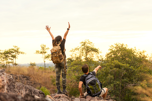 Hiker couple backpack pointing and sitting happy feeling freedom good and strong weight victorious facing on the natural mountain. Traveler going camping outdoors destination leisure