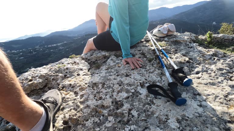 Mature female hiker relaxes at summit viewpoint above distant mountains