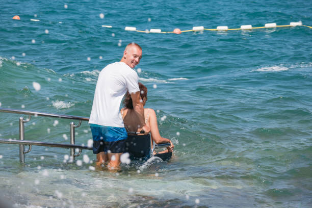 Woman with disability on wheelchair at accessible beach goes swimming.