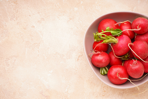 Fresh red radish in a bowl on a beige background, closeup, space for text. Fresh red radish.