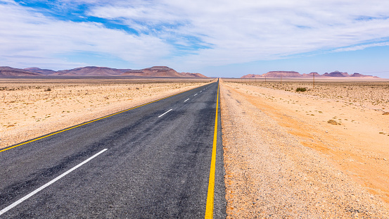 A tarmac highway cuts through the dry, arid landscape of the Namib Desert near Aus, Namibia.  Horizontal.